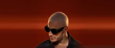 DJ Snake wearing sunglasses against a deep red background, featured on Lickd for music licensing
